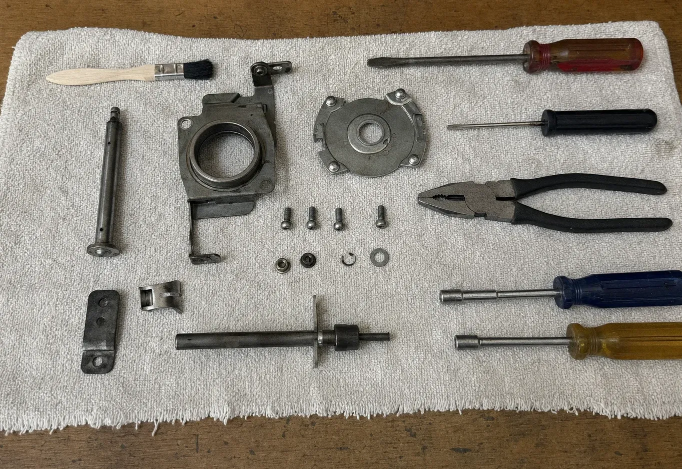 Burner base casting, a round burner head, a spindle, hinge parts, pliers and screwdrivers laid out on a towel